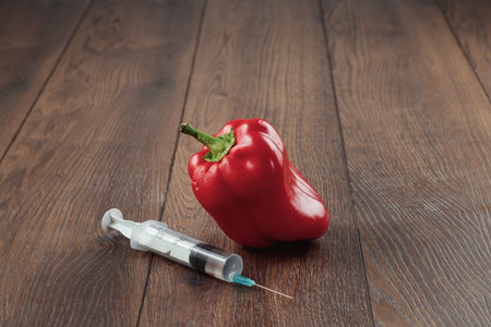 Red pepper and stuck in it a syringe on a wooden background. Concepts of genetic modification....