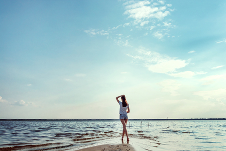 Young, beautiful girl stands against the sky and big lake. The concept of travel, clean air, a lot of free space, a distant horizon.の写真素材
