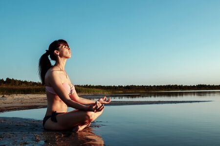 Young girl silhouette, yoga on nature, on a background of a lake and beautiful sunset. Fresh air, healthy way of life,の写真素材