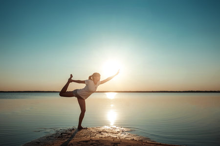 Young girl silhouette, yoga on nature, on a background of a lake and beautiful sunset. Fresh air,...