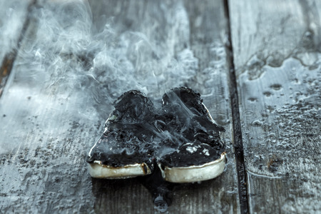 Creative background, burning shoes on a wooden background. The concept of sweat feet, bad smell, spoiled shoes after long use.の写真素材