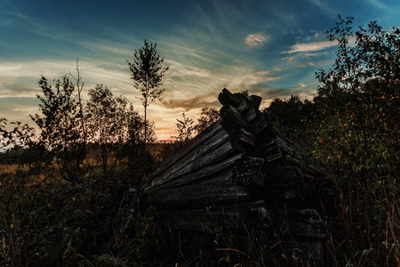 Creative background, ruined wooden house on a background of beautiful sunset. The concept of a magical background, fantasy, mysticism, devastation, old age.の写真素材