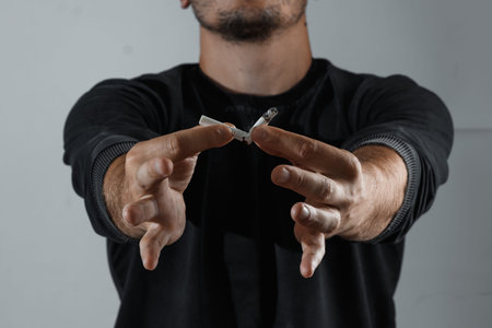 A man on a dark background breaks a cigarette. The concept of quitting smoking, giving up a bad habit.の写真素材