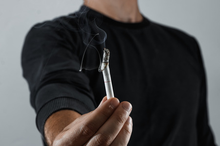 A man holds a cigarette in his hand and smokes extremely close-up. The concept of smoking. The burning of cigarettes between the fingers of a young man is shallow with a copy of the depth of field.の写真素材