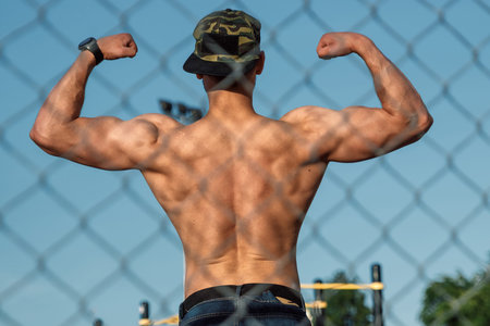 A young muscular guy with a bare torso resting after training, an athlete, outdoor training in the...