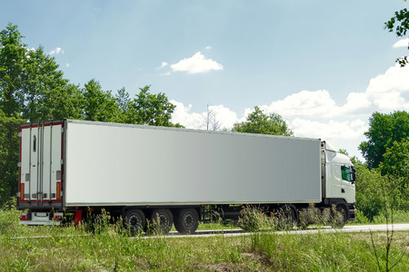 White truck driving on the asphalt road next to the green field in rural landscape at sunsetの写真素材
