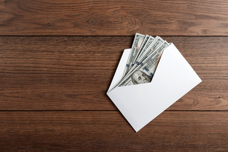 US dollars in a white envelope on a wooden table. The concept of income, bonuses or bribes....
