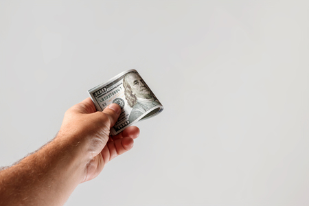 US dollars in a male hand on a light background. Concept Bribe, additional work, salary, bonus, bonus, cache back.の写真素材