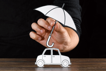 The concept of car insurance, a man covers a car with paper hands, close-up.の写真素材