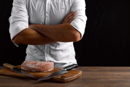 Hands of the chef close-up, folded hands on a dark background. The concept of cooking, cooking meat, a recipe for meat dishes.の写真素材