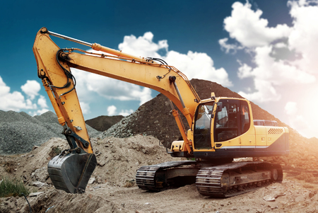 Excavator at the construction site, sand, crushed stone, against the blue sky background. Construction equipment, construction.