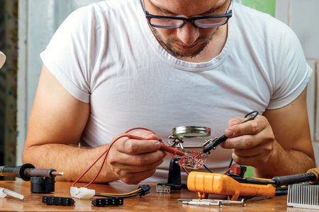 The man remotes the microcircuit. Workplace with soldering iron, microcircuit, magnifying glass,...