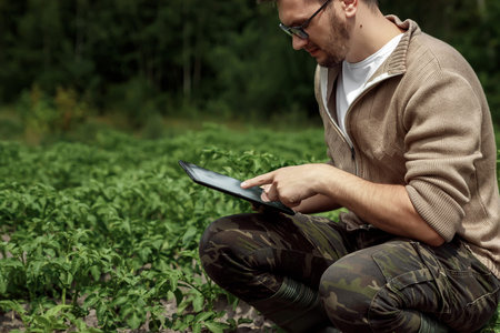 A male farmer sitting in the field and using a tablet. Modern application of technologies in...