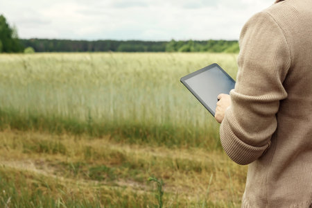 A farmer standing in the field and using a tablet. Modern application of technologies in...