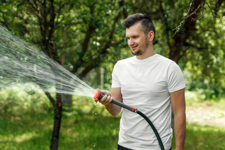 A man is watering from a hose, the concept of gardening. Hand held garden hose with water spray,...