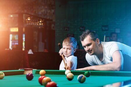 Father and son play billiards. The father teaches his son to play billiards. The concept of parents and children, upbringing, family rest.の写真素材