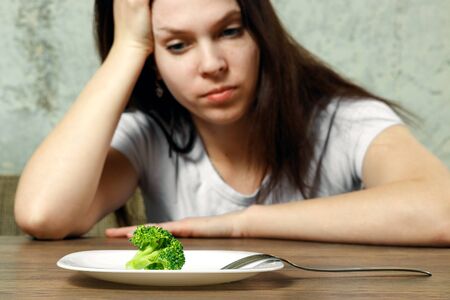 sad young brunette woman dealing with anorexia nervosa or bulimia having small green vegetable on plate. Dieting problems, eating disorder.の写真素材