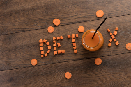 Inscription detox, carrot juice in a glass on a wooden background, top view. Concept of healthy eating, raw food diet, diet.の写真素材