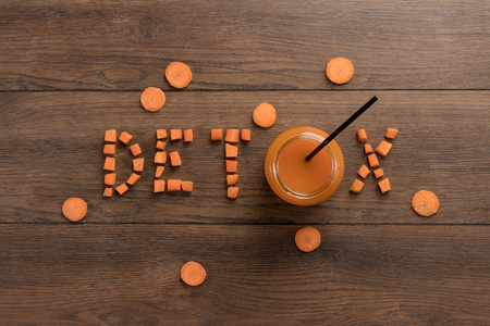 Inscription detox, carrot juice in a glass on a wooden background, top view. Concept of healthy eating, raw food diet, diet.の写真素材