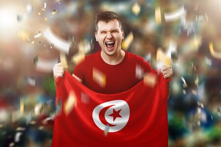 Tunisian fan, fan of a man holding the national flag of Tunisia in his hands. Soccer fan in the stadium.の写真素材