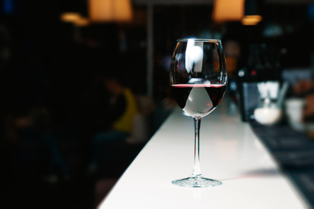 A glass of red wine close-up on a bar, white counter. Dark background.の写真素材