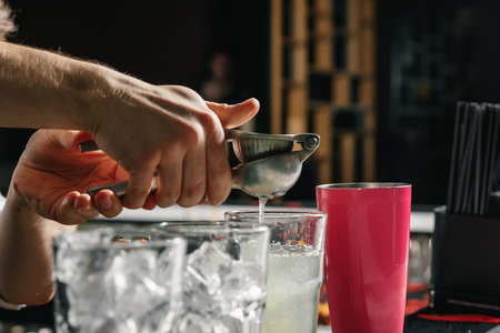 Male hands of the bartender close-up, makes a cocktail on the bar, glasses with ice.
