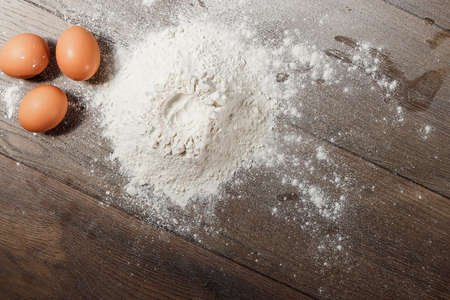 Top view of the egg, flour, a glass of fresh milk, cooking dough on the background of a wooden table. Flat layの写真素材