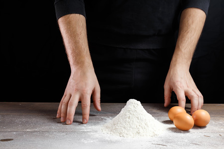 Male hand chef close-up. Preparation of Italian food pasta, pizza or bread focaccia. The recipe for cooking home-made dishes from the chef. Dark background.の写真素材