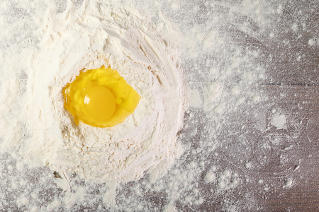 The top view of an egg, beaten into flour, cooking dough against the background of a wooden table. Flat layの写真素材