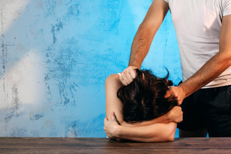 A man mocks a woman against a blue wall. Concept of domestic violence