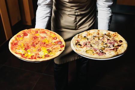 Waiter carrying two different plates with a tasty pizza. Photo with two pizza. Pizza with mushrooms and pizza with salami. Italian food. Italian restaurant.の写真素材
