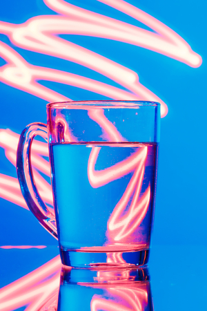 Glass of water on a blue background with a yellow abstraction, glare of light.の写真素材