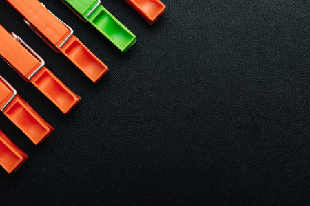 One green, linen clothespin in a row of orange, linen clothespins on a black background. Creative...