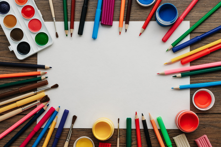 A white sheet of A4 paper lies on a wooden brown table next to paints, brushes, colored pencils. View from above. The concept of creativity, creative, drawing.の写真素材