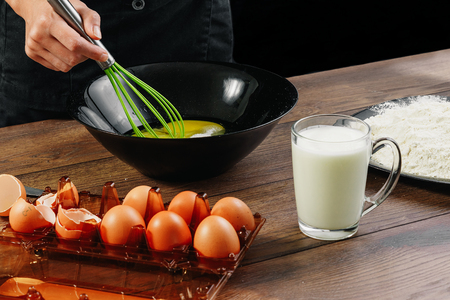 Whipping eggs. Chef hands close-up whisk eggs on a black background. Natural light, slightly toned image. Copy space.の写真素材