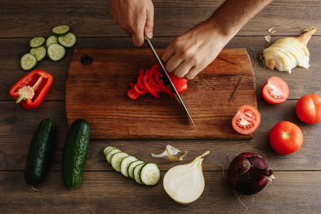 The chef cuts fresh and tasty vegetables for cooking. Hands close-up. View from above. Wooden brown background. Beautiful food still life.の写真素材