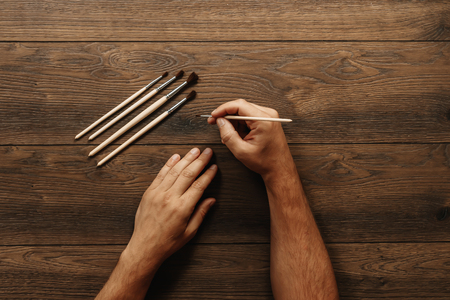 Male hands hold tassels on a brown wooden background. Close-up, top view. The concept of creativity, drawing. .の写真素材