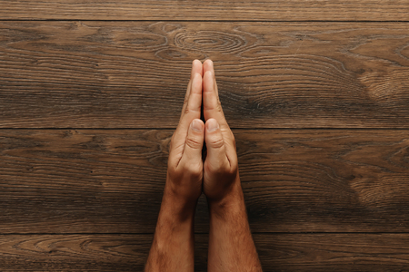 Male hands are folded in prayer on a wooden brown background.の写真素材