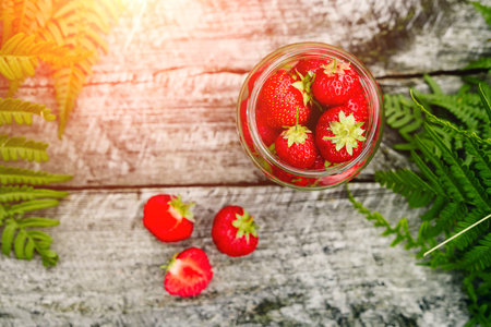 Strawberries in a glass jar on a wooden gray table on a green background, leaves of paparatnik, strawberry season. opy space for text,の写真素材