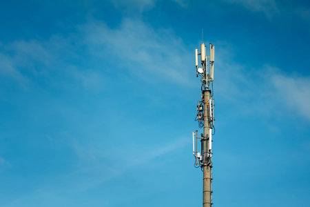 Telecommunications mast set against blue sky and big white cloud