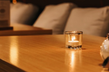 A small candle burns in a glass on a wooden tableの写真素材