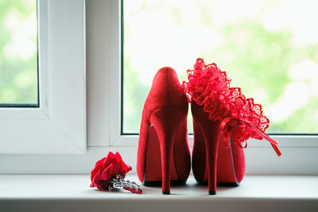 Red women's shoes stand on the windowsill, wedding, boutonniere.の写真素材