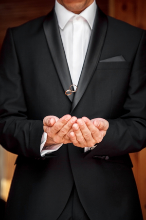 A stylish bridegroom in a black suit tosses wedding gold rings from her handsの写真素材