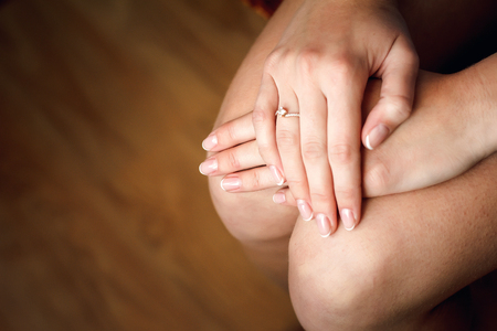 A girl in a silk robe sits on a chair and crosses her hands on her knees.