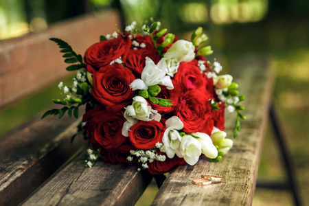 Gold wedding rings on a wooden bench on the background of a beautiful wedding bouquetの写真素材