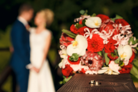 Golden wedding rings on the background of a wedding bouquet of red rosesの写真素材