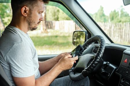 A man at the wheel holding a smartphone in his hand, violates traffic rules. The concept of an accident, a traffic violation, the phone at the wheel.の写真素材