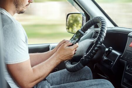 A man at the wheel holding a smartphone in his hand, violates traffic rules. The concept of an accident, a traffic violation, the phone at the wheel.の写真素材