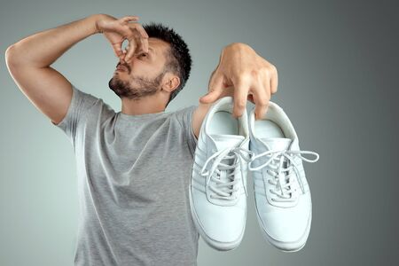 A man holds sneakers in his hands. Nasty smell. Stink legs, fungus on the legs.の写真素材