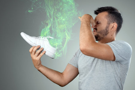 A man holds sneakers in his hands. Nasty smell. Stink legs, fungus on the legs.